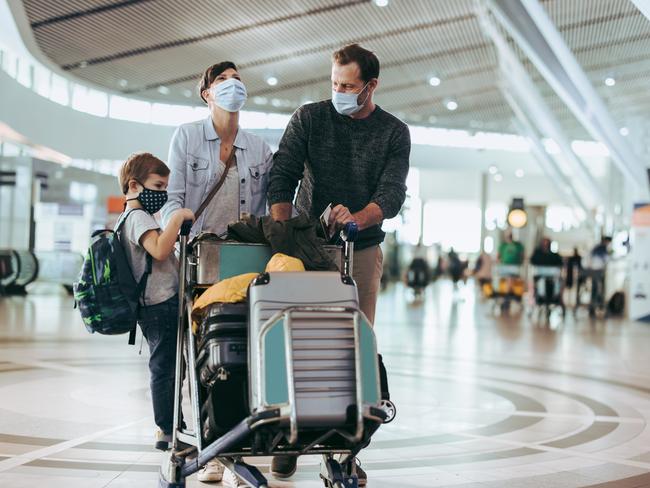 Couple with child standing on luggage trolley at airport. Passport delays are causing massive stress.