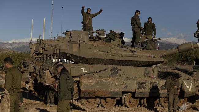 Israeli soldiers stand near a tank as it is moving along the border with Lebanon.