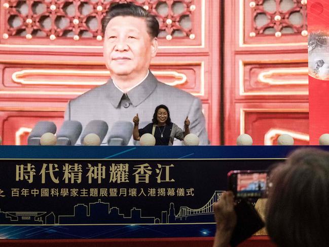 In this picture taken at the Hong Kong Convention and Exhibition Centre in Hong Kong on July 8, 2021, a visitor poses for photos at an exhibition celebrating the 100th anniversary of the founding of the Communist Party of China in front of a large screen showing Chinese President Xi Jinping. - This month was the first time high-profile events had been put on for a party anniversary in Hong Kong. (Photo by Anthony WALLACE / AFP) / TO GO WITH HongKong-China-politics,FOCUS