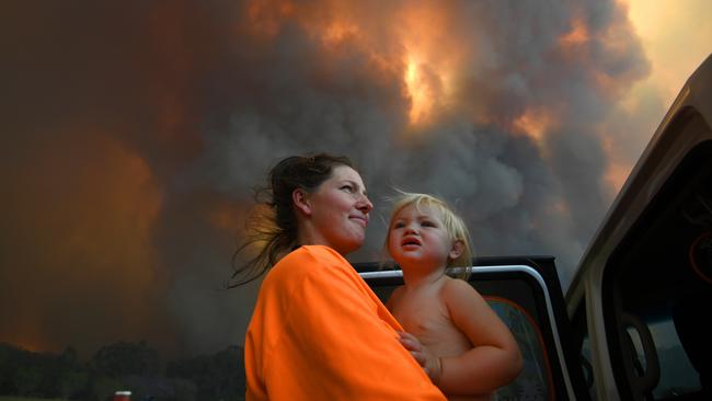 Sharnie Moren and her 18 months old daughter Charlotte look on as thick smoke rises from bushfires in Nana Glen, near Coffs Harbour. Picture: AAP Image/Dan Peled