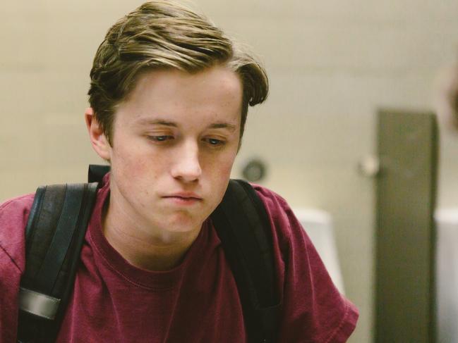 Depressed teen student helplessly stares at his reflection in bathroom mirror.