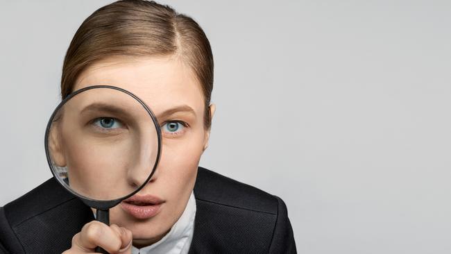 Portrait of a girl in the office at work looks carefully into the magnifying glass with one eye. The concept of office work and search. tax generic