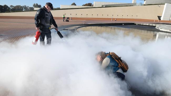 A policeman uses a fire extinguisher to put out a pram that was on fire while a young female protester sits on the Parliament forecourt. Picture: Gary Ramage