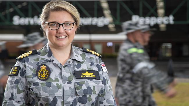 HMAS Cerberus Recruit School Commanding Officer, Commander Alisha Withers, RAN, standing within the Recruit School grounds as recruits march past conducting drill training.