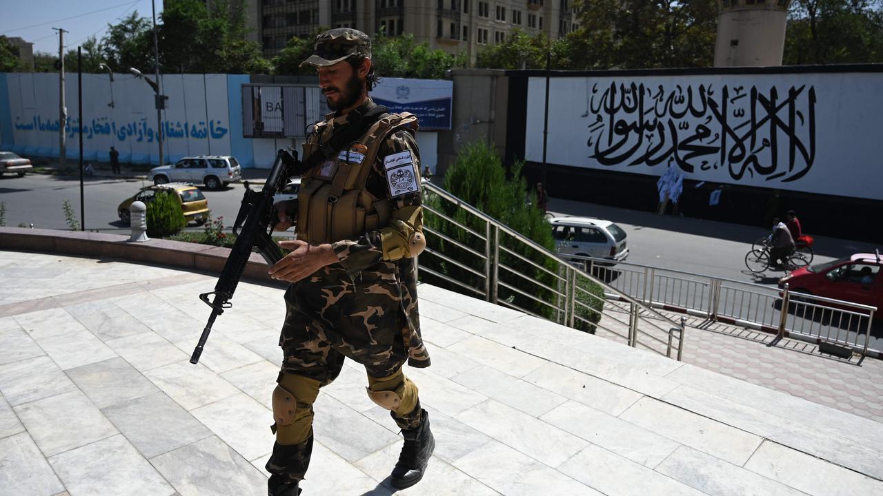 A member of the Taliban Fateh fighter stands guard outside the US embassy in Afghanistan displaying a Taliban flag in the outer concrete wall. Picture: AFP