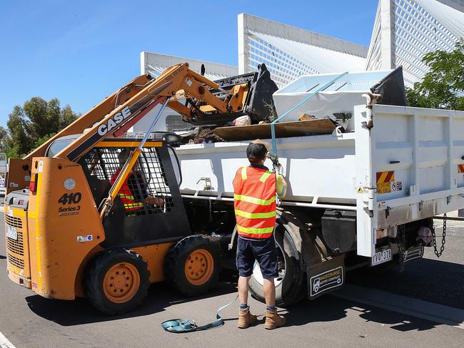 Workers clean up around the Ecoville Community Centre in Tarneit as police monitor the area. Picture: Ian Currie