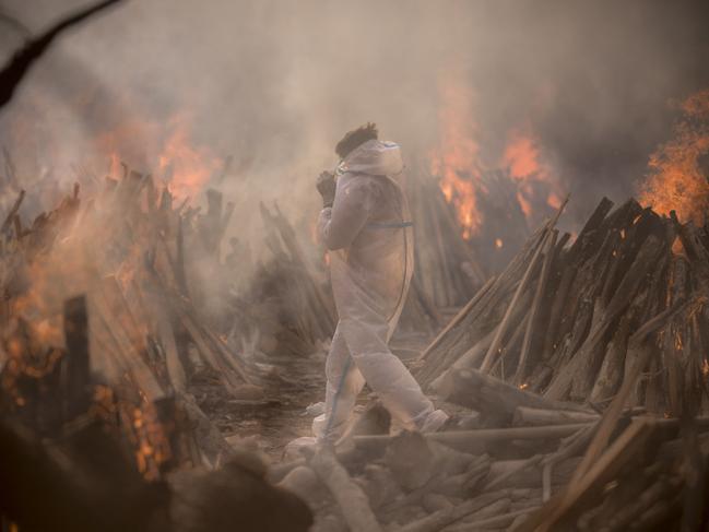 A worker in PPE amid the burning funeral pyres of patients who died of COVID-19 at a crematorium in New Delhi, India. Picture: Getty Images