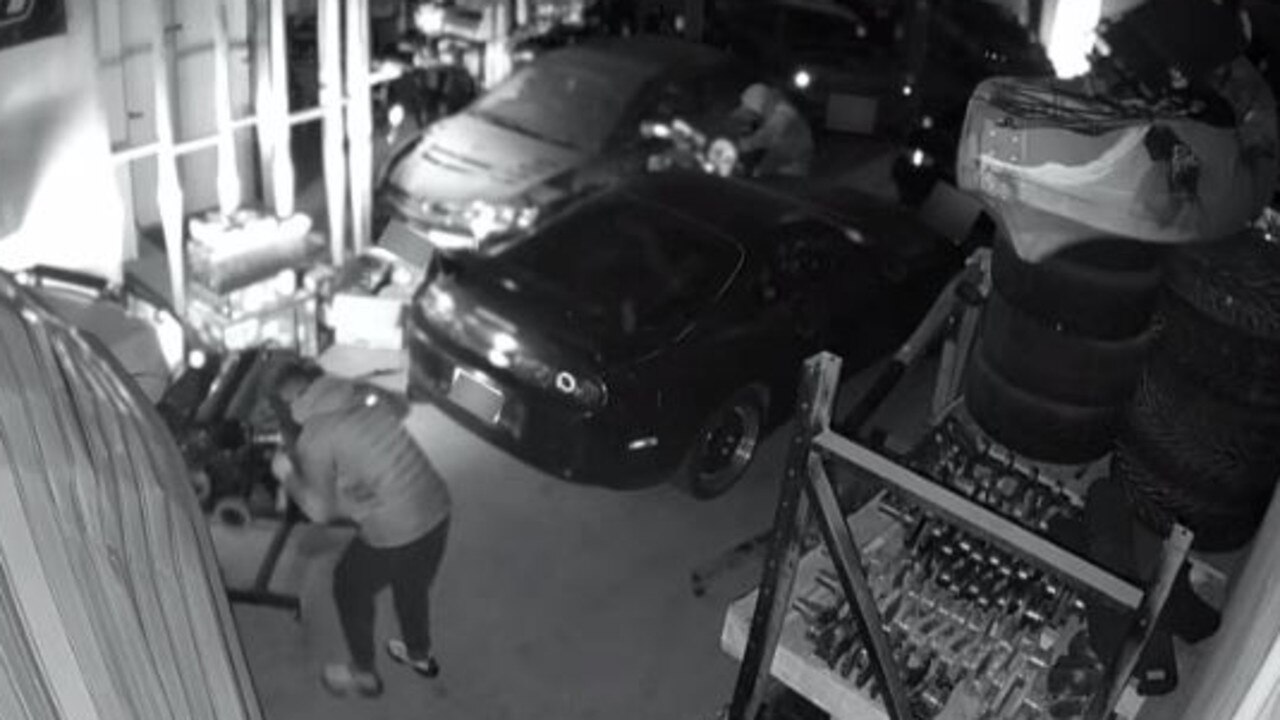 Footage shows two men wheeling car engines out from the shop and under the buckled door. Picture: Supplied