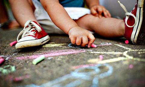Close up of little boy in canvas shoes drawing with chalks on the sidewalk