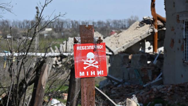 A warning sign which reads "dangerous mines" placed near destroyed houses during a demining operation in Grakove Village, Kharkiv region.