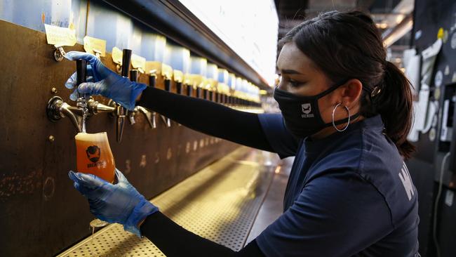 A bartender poors a beer while wearing personal protective wear at BrewDog Tower Hill. Picture: Getty Images