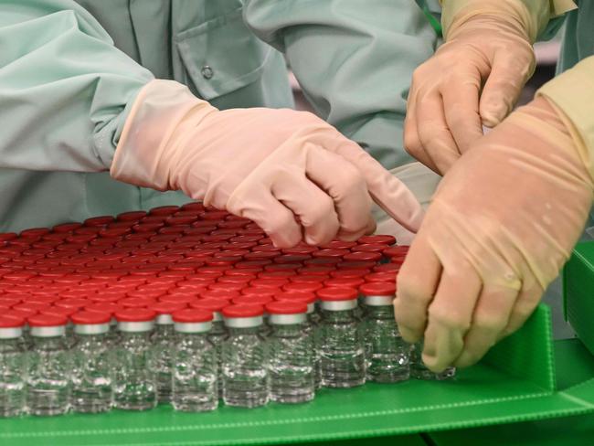 Lab technicians handle capped vials as part of filling and packaging tests for the large-scale production and supply of the University of Oxford’s vaccine. Picture: AFP