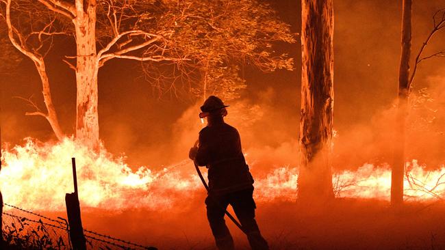 A firefighter desperately hoses down trees and flying embers in an effort to secure nearby houses from bushfires near Nowra on New Year's Eve. Picture: Saeed Khan/AFP