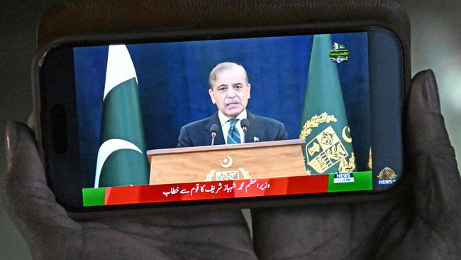 A resident watches his smartphone as Pakistan's Prime Minister Shehbaz Sharif addresses the nation from Islamabad. Picture: Aamir Qureshi/AFP