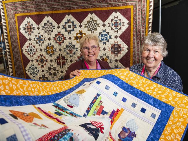 Toowoomba Quilters Club members Christina Pierpoint (left) and Bev Bain hold a community quilt that will be donated in front of a queen bed quilt the club is raffling to raise funds for Isolated Children's Parents' Association on display at Craft Alive. Picture: Kevin Farmer