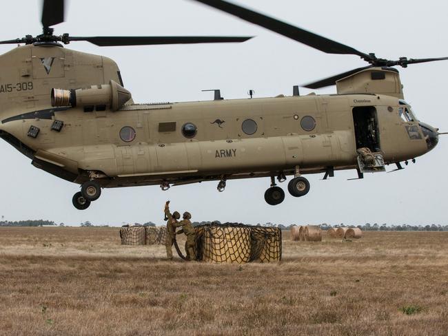 Lance Corporal Jesse Ablett and Private Matt Crabtree work together to hook a load of three round hay bales under an Australian Army CH-47 Chinook helicopter as it hovers above them as part of an animal feed drop at Bairnsdale airport, Victoria.