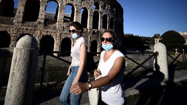 People observe the new rule on wearing face masks as they walk past the Colosseum in Rome. Picture: AFP