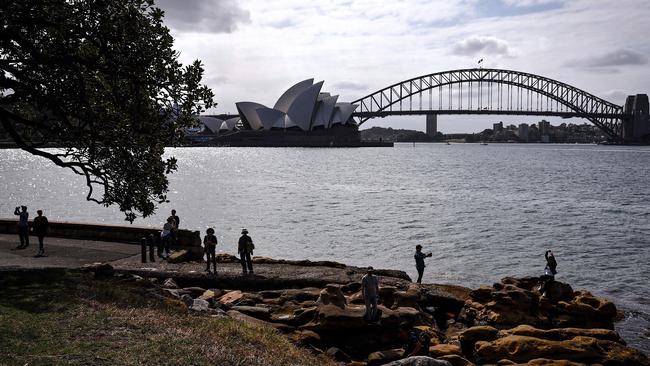 Tourists stand on rocks as they take photographs in front of the Sydney Opera House and Sydney Harbour Bridge. Picture: AFP