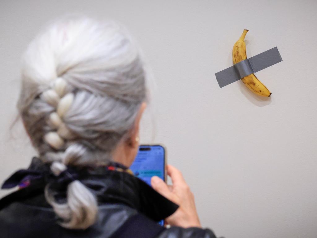 (FILES) A journalist takes a picture of Italian visual artist Maurizio Cattelan's duct-taped Banana entitled "Comedian," displayed during a media preview at Sotheby's in New York, on November 8, 2024. A fresh banana taped to a wall -- a provocative work of conceptual art by Italian artist Maurizio Cattelan -- was bought for $6.2 million on November 20, 2024 by a cryptocurrency entrepreneur at a New York auction, Sotheby's announced in a statement. The debut of the edible creation entitled "Comedian" at the Art Basel show in Miami Beach in 2019 sparked controversy and raised questions about whether it should be considered art -- Cattelan's stated aim. (Photo by kena betancur / AFP) / RESTRICTED TO EDITORIAL USE - MANDATORY MENTION OF THE ARTIST UPON PUBLICATION - TO ILLUSTRATE THE EVENT AS SPECIFIED IN THE CAPTION / TO GO WITH AFP STORY BY Ana FERNANDEZ: "Magritte, Rucha and... a banana, in a bid to set new records at New York auctions"