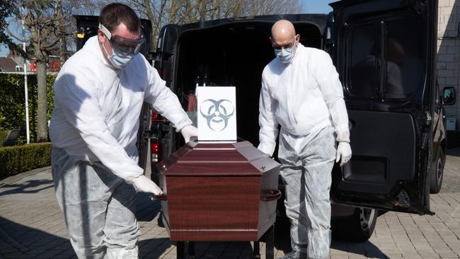 Two workers in Belgium wearing protective gear carrying a coffin at an unknown funeral service company. Picture: Benoit Doppagne