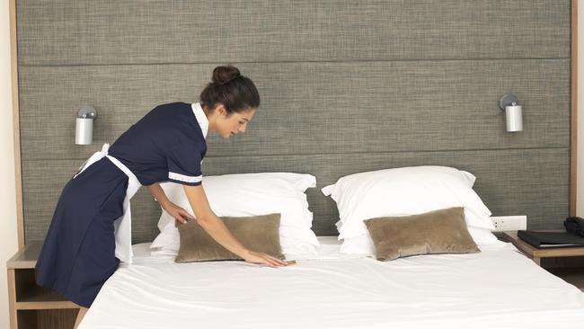 Generic image of a housekeeper making a bed in a room of a hotel.