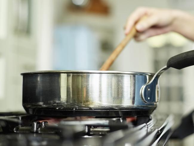 Midsection below view image of woman cooking food in pan. Utensil is placed on gas stove. Female is stirring dish in frying pan. She is preparing food in domestic kitchen.