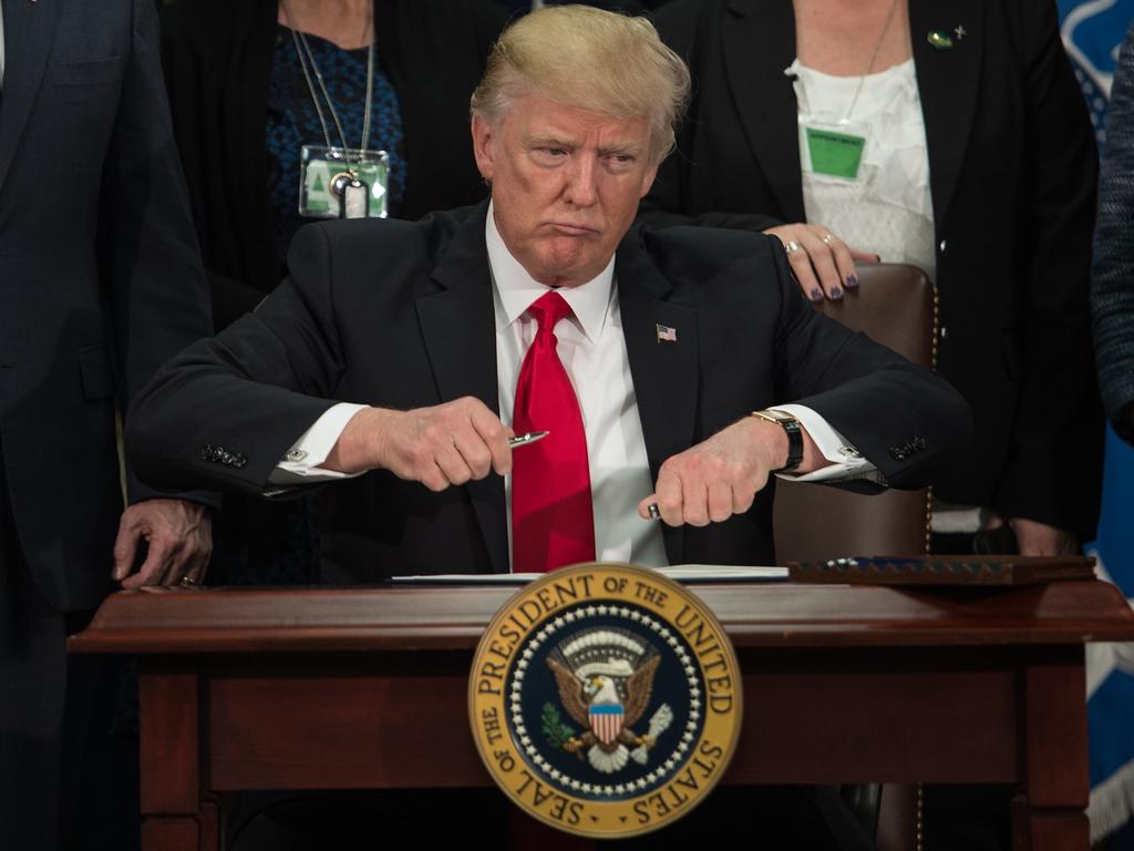 Donald Trump takes the cap off a pen to sign an executive order to start the Mexico border wall project at the Department of Homeland Security facility in Washington, DC. Picture: AFP