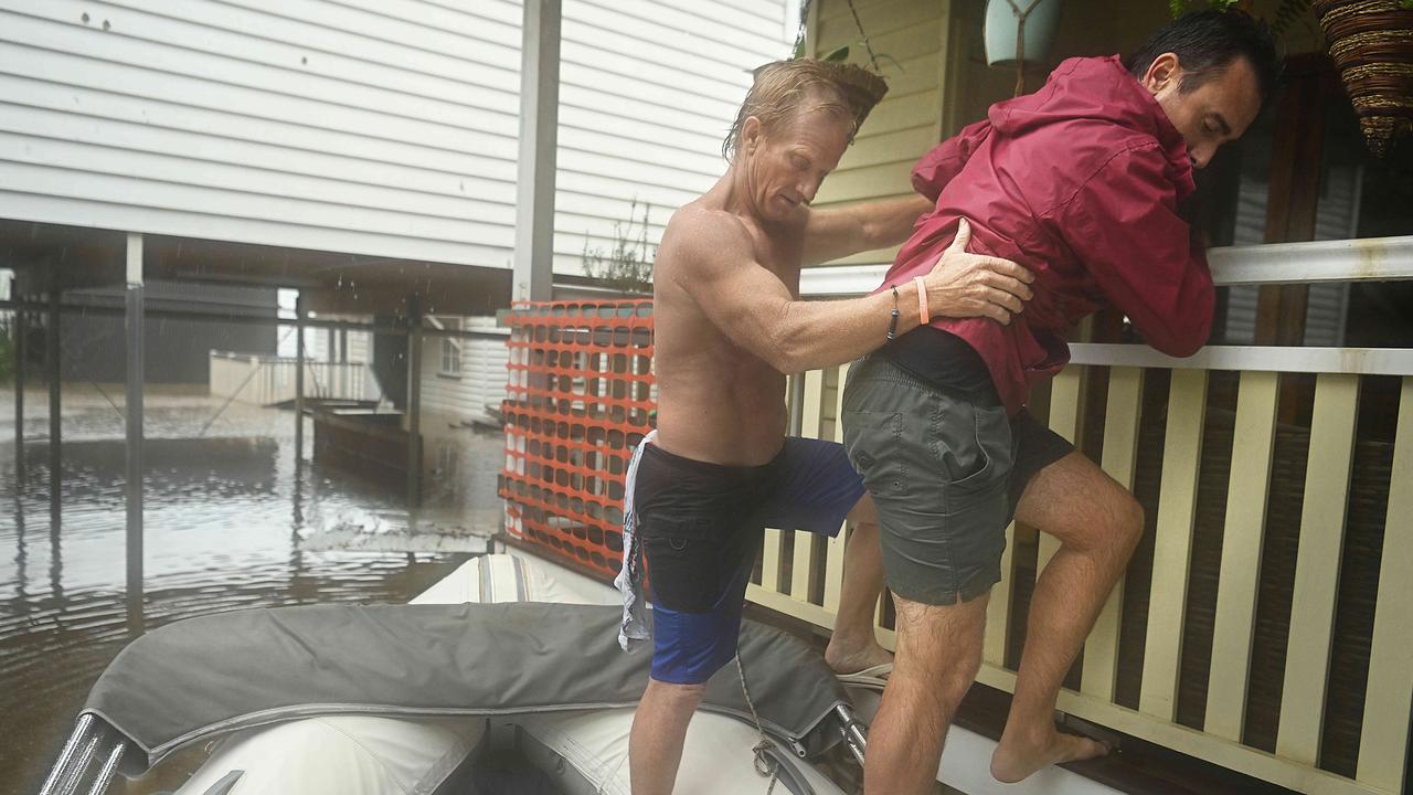 Resident Andy Smith (in red) is helped from his flooded house by Craig Harris by boat driven by David Millar as flood waters engulf Torwood and Vincent St and houses in Auchenflower, Brisbane. Pic Lyndon Mechielsen