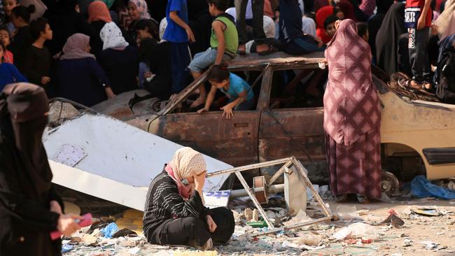 Children play in a charred car as people queue for bread in front of a bakery that was partially destroyed in an Israeli strike, in the Nuseirat refugee camp in the central Gaza Strip. Picture: AFP