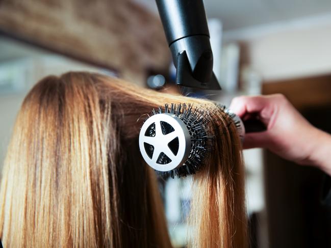 Professional woman hairdresser making hairstyle using hair dryer for young female in beauty salon. For: Where, why and when in 2020. Credit: Istock