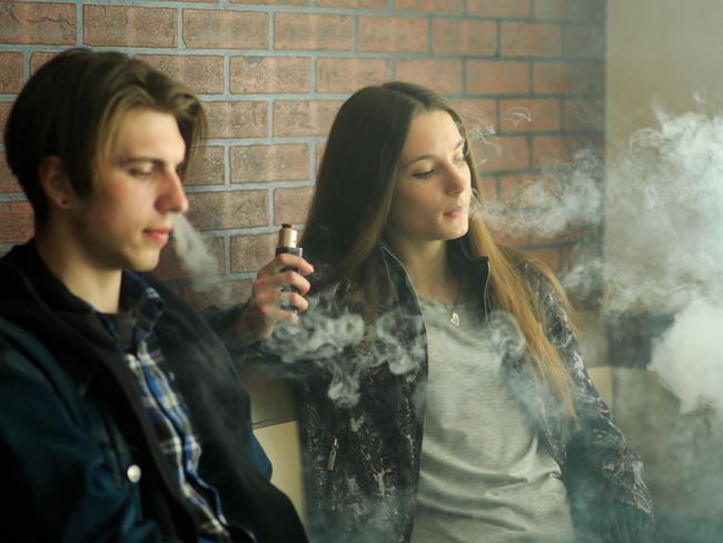 Vape teenagers. Young cute girl in sunglasses and young handsome guy smoke an electronic cigarettes in the vape bar. Bad habit that is harmful to health. Vaping activity.