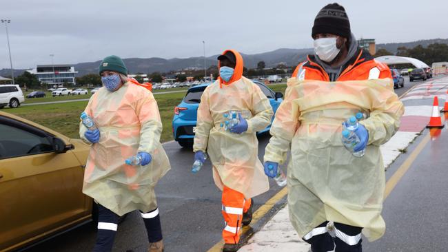 People hand out bottled water to motorists queuing in the cold and the rain at the Victoria Park drive-through testing site. Picture: Emma Brasier