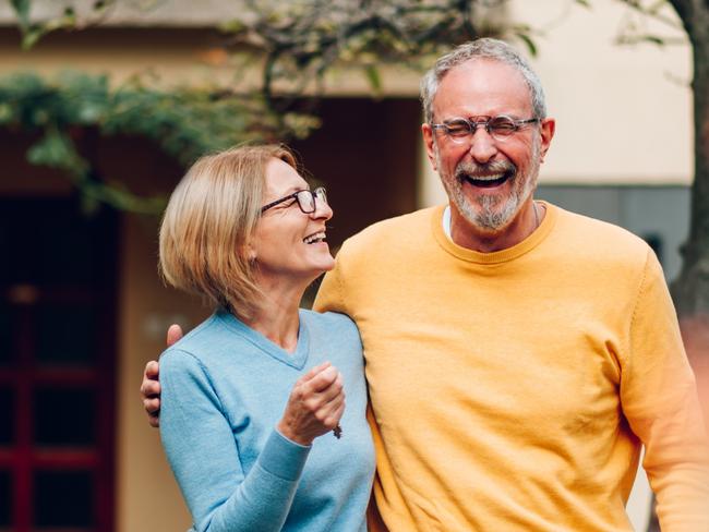 Portrait of a senior married couple holding keys and standing outside their new home on a moving day and hugging. Mature people outside their new house. Copy space. Investing in property.