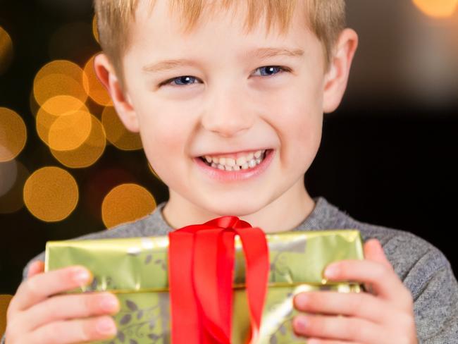 Excited little boy holding Christmas gift near tree