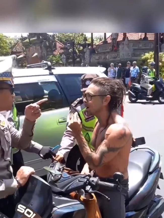 A shirtless Bali tourist on a scooter was confronted by police for not wearing a helmet in a tense exchange on the side of a busy road.