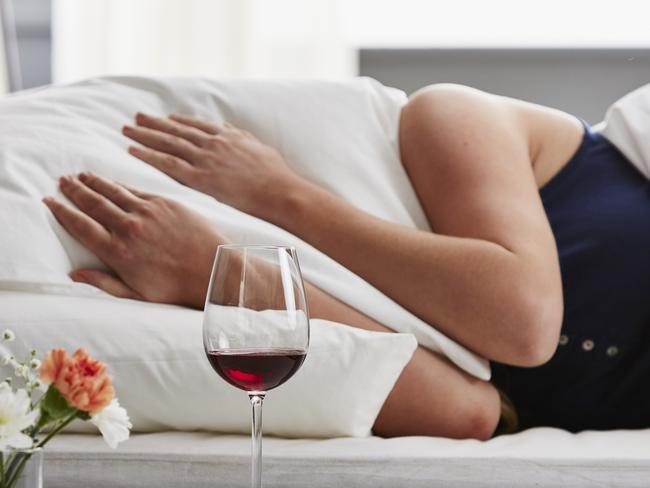 Woman lying in bed, head under the pillow suffering with a hangover