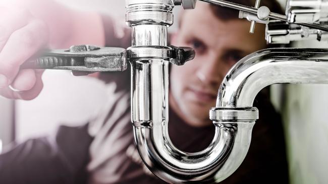 TRADESMAN:  CAREERS: Plumber using a wrench to tighten a siphon under a sink.