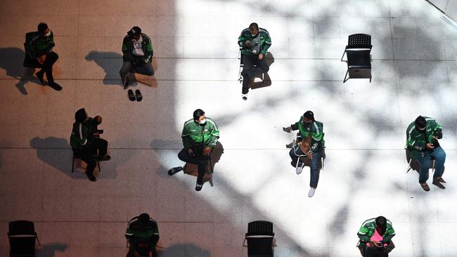 A group of Grab Food delivery drivers sit on chairs spaced apart for social distancing as they wait for takeaway orders at Central Pinklao shopping mall in Bangkok.