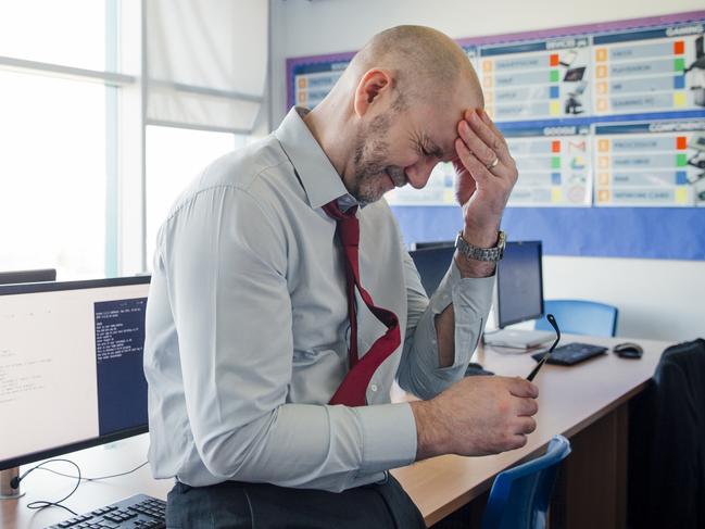 Stressed, concerned teacher sits on the edge of a desk in an empty classroom, schools, upset. Istock