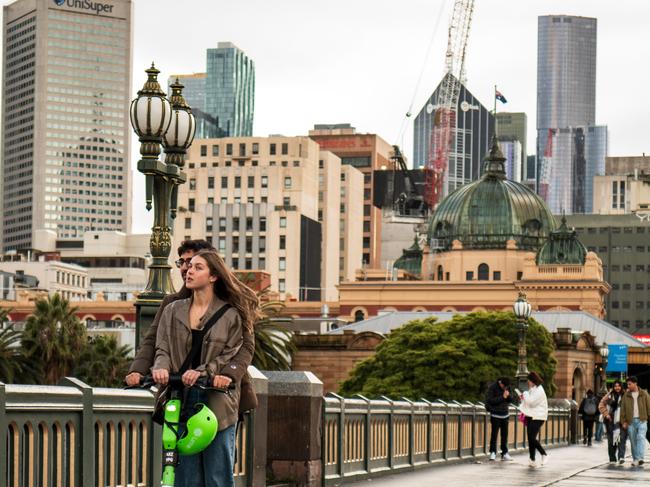 MELBOURNE, AUSTRALIA - NewsWire Photos. JULY 28: Pedestrians cross Princes Bridge with Melbourne's skyline in the background during a cold and wet day as the city experiences an icy blast on July 28, 2024 in Melbourne, Australia. Picture:  NewsWire / Tamati Smith