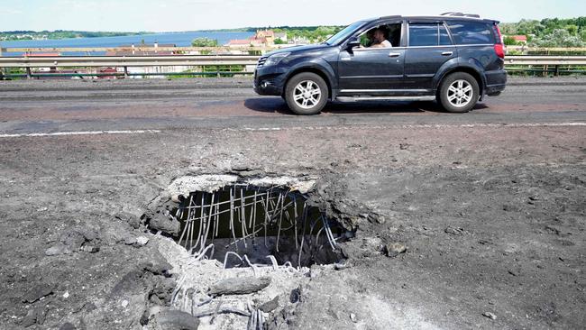 A driver passes a crater on Kherson's Antonovsky bridge across the Dnipro river in Ukraine caused by a rocket strike. Picture: AFP