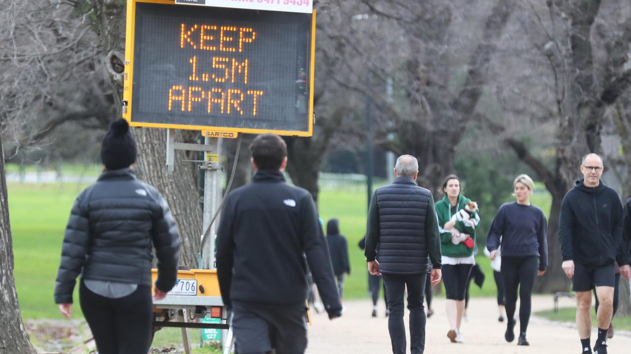 People pass a warning sign while exercising in Melbourne during the second COVID-19 lockdown. Picture: David Crosling