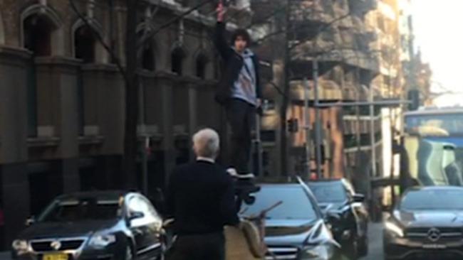 The knife-wielding man stands on a car as a member of the public approaches him armed with only a chair. Picture: Seven News