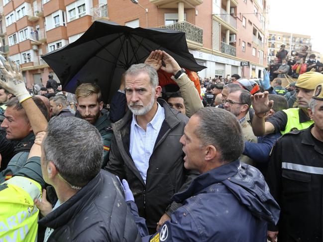 Spain's King Felipe VI is protected after a crowd of angry survivors of Spain's floods tossed mud and shouted insults. Picture: AP