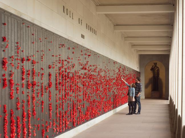 "Canberra, Australia - November 12, 2012: A young woman points as she and her male companion walk past rows of poppies placed on the Wall of Remembrance at the Australian War Memorial. The poppies are placed to honour Australian soldiers who have lost their lives in war or during military service."