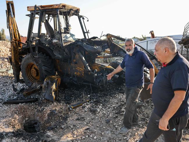 Men walk past a hole in the ground and a burnt tractor after a rocket fired from southern Lebanon hit the town of Kfar Manda in northern Israel. Picture; AFP.