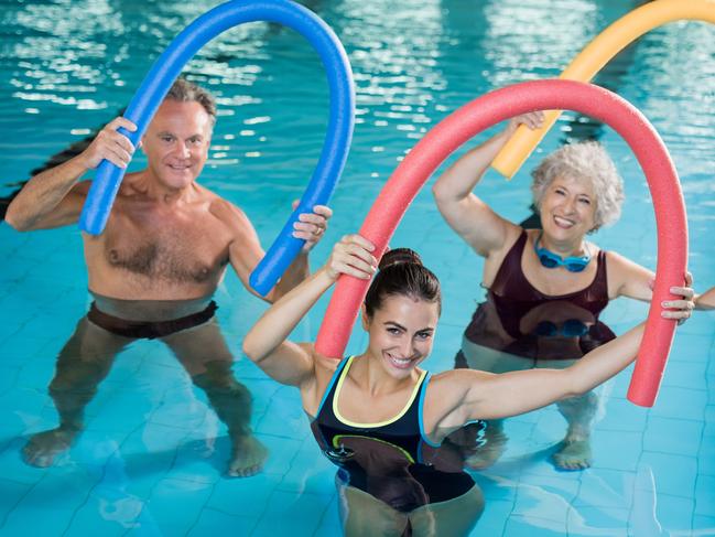 Portrait of smiling people doing aqua fitness together in a swimming pool. Group of senior woman and mature man with swim noodles exercising in a swimming pool. Young trainer and senior people in aqua gym fitness class.