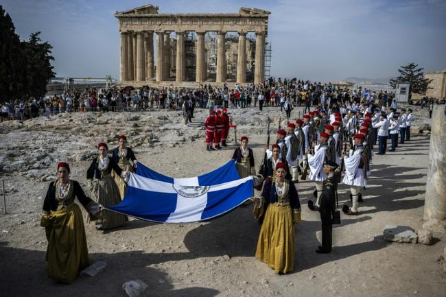 Traditionally attired women carry a Greek flag on Acropolis hill during the liberation commemoration