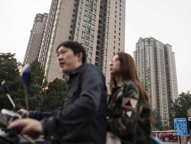 A man and woman sit on a scooter in front of the residential luxury homes of Guangcai (top) in Beijing's Chaoyang district on September 29, 2016. China's richest man, real estate magnate Wang Jianlin, has warned the country's property market is the 