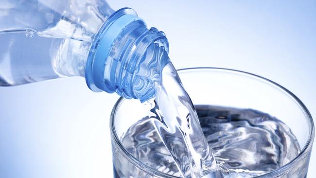 Close-up Pouring glass of water from a plastic bottle on blue background